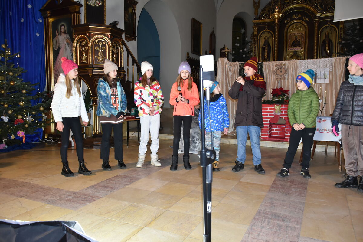 W kościele dzieci ze Szkoły Podstawowej w Zembrzycach przedstawiają opowieść wigilijną. Stoją obok siebie, z przodu nagrywa telefon.