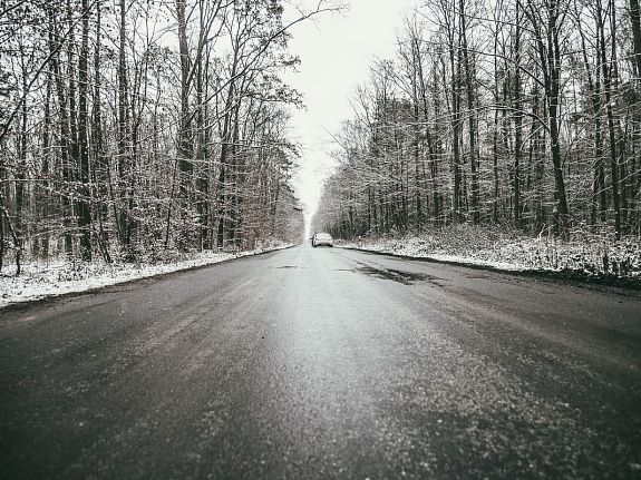 oblodzona droga asfaltowa. na drugim planie las, drzewa oprószone śniegiem.
